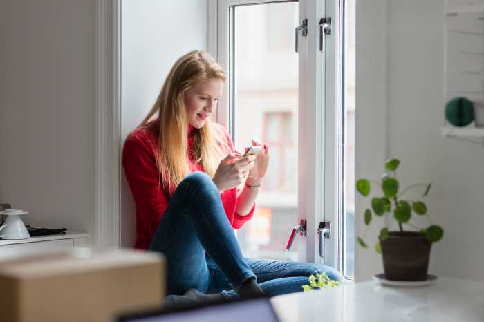 Kvinde sidder i et vindue med en mobiltelefon
