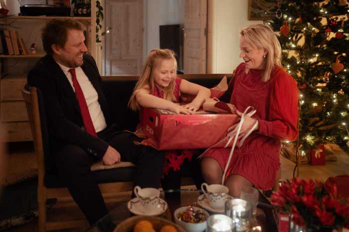 Et barn sidder mellem en mand og en kvinde i en sofa juleaften og åbner en julegave
