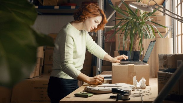 en kvinde står på et lager med sin bærbare computer og tager noter i en notesblok