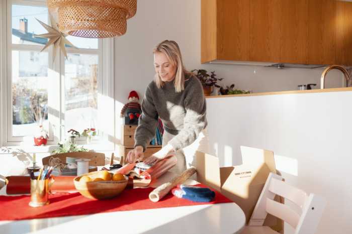 En kvinde læner sig smilende over et bord og pakker en sweater i julegave.