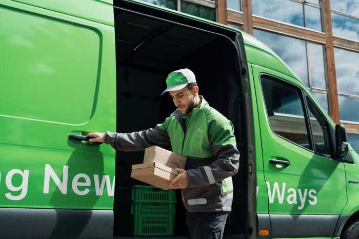 En Bringbud står med pakke i hånden ved siden af en åben Bring-bil