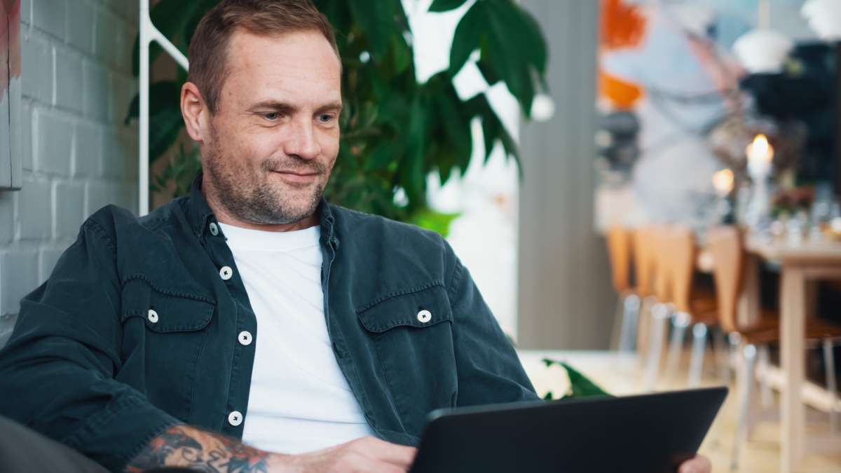 En mand sidder på en sofa med en bærbar computer på skødet