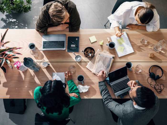 Fire mennesker sitter ved et bord med laptoper, kaffekopper og skriveblokker.