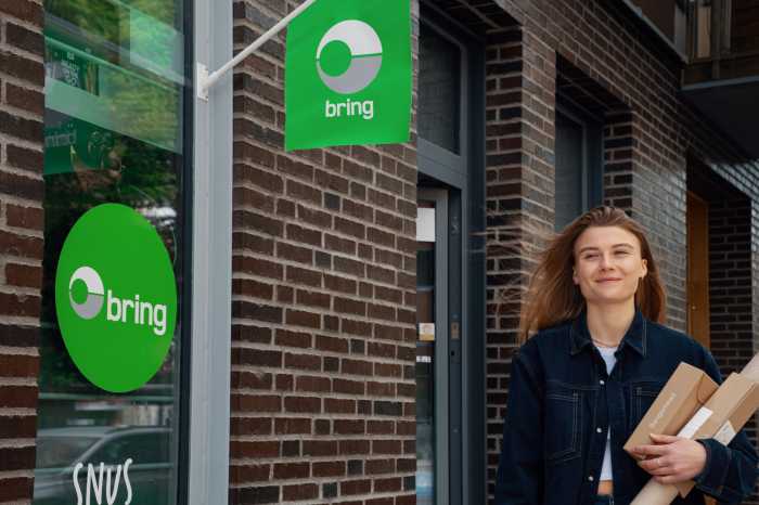 En kvinde står med en pakke i hånden uden for et Bring udleveringssted