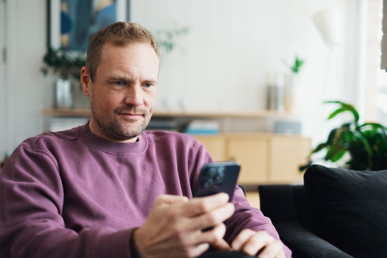 En mand sidder og kigger på en mobiltelefon, som han holder i hånden