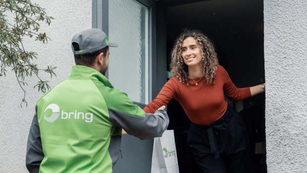En Bringbud står foran et hus og afleverer en levering til en kvinde, der står i døren