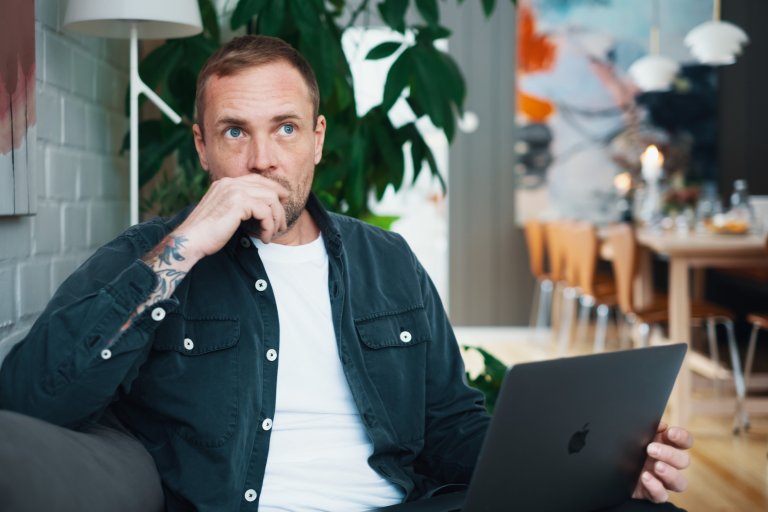 En mand sidder på en sofa med en bærbar computer på skødet og ser eftertænksom ud