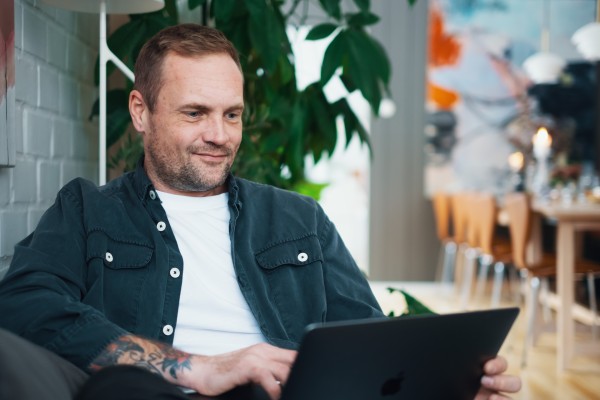 En mand sidder på en sofa med en bærbar computer på skødet