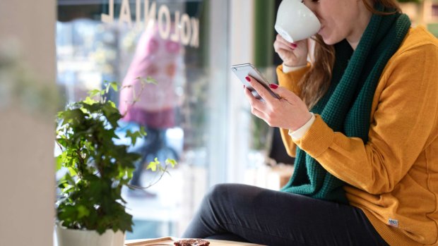 en kvinde drikker kaffe og kigger på sin mobiltelefon