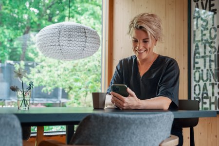 Kvinde sidder ved et bord og smiler til mobiltelefonen